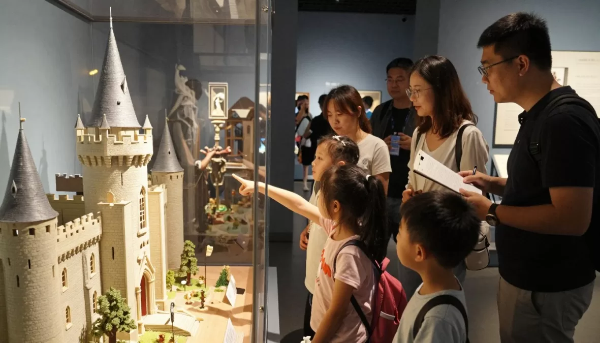 Museum visitors viewing Astolat Dollhouse Castle exhibition with children looking through windows