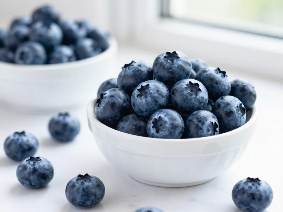 Fresh blueberries in a white bowl with scattered berries on a marble surface