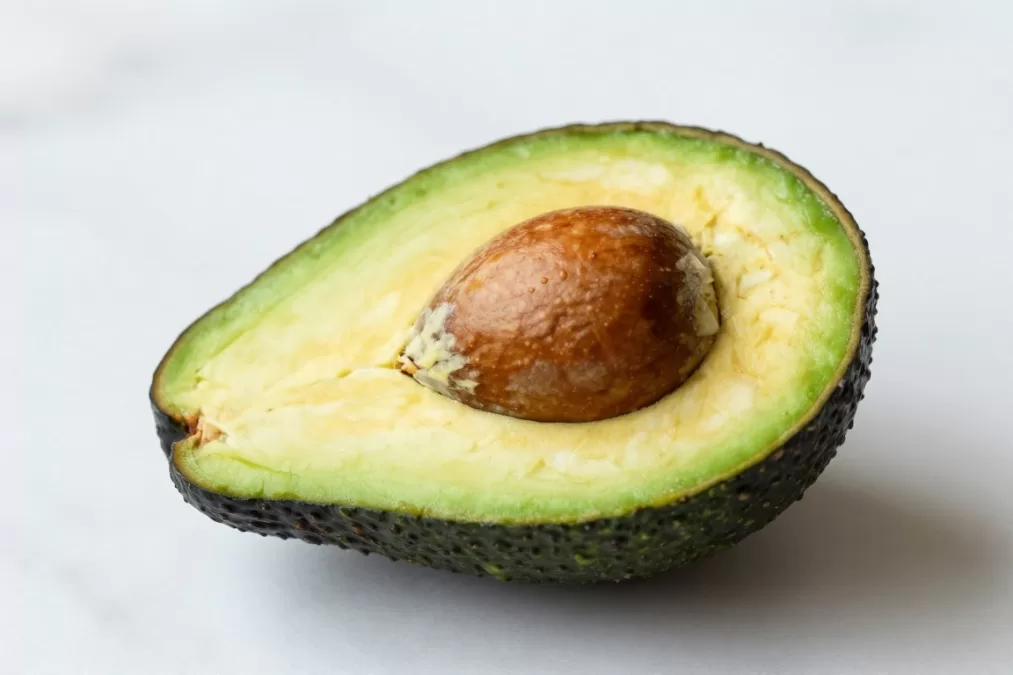 Halved avocado showing creamy green flesh and pit on white marble surface