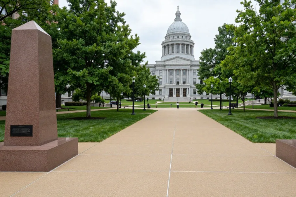 Long public park walkway flanked by granite monuments, trees, and a distant neoclassical state capitol building Long public park walkway flanked by granite monuments, trees, and a distant neoclassical state capitol building